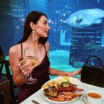 Woman dines amongst the fish at the world famous Cargo hold restaurant in Durban South Africa as featured on the durbanvibe.co.za what's on in durban and Durban tourist information website